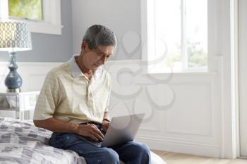 Senior Man Sitting On Bed Using Laptop Computer