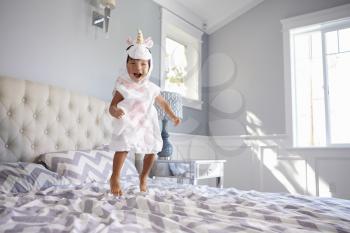 Girl Dressed In Unicorn Costume Jumping On Bed At Home