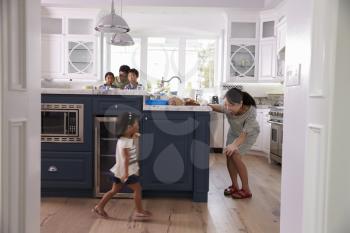 Parents Prepare Food As Children Play In Kitchen