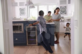 Parents Prepare Food As Children Play In Kitchen