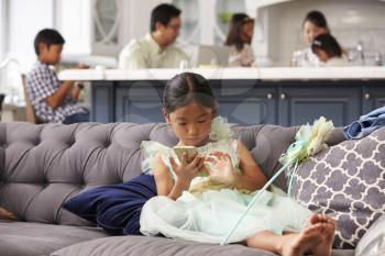 Young Girl Sitting On Sofa Using Mobile Phone At Home
