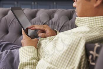 Man Relaxing On Sofa At Home Using Digital Tablet