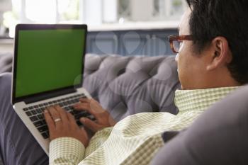 Man Relaxing On Sofa At Home Using Green Screen Laptop