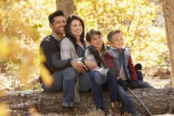 Happy family sitting on fallen tree in a forest looking away