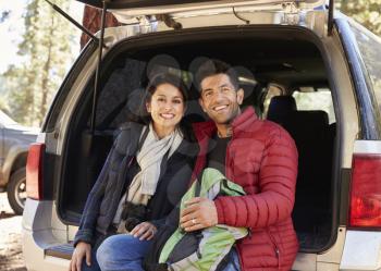 Happy Hispanic couple sitting in open back of car before hike