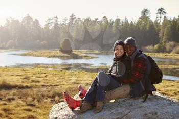 Mixed race couple on a rock in countryside looking to camera