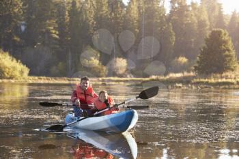 Father and son kayaking on rural lake, front view