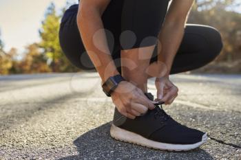 Woman tying her sports shoe in street, low section close up