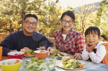 Asian parents and daughter at a table outdoors look to camera
