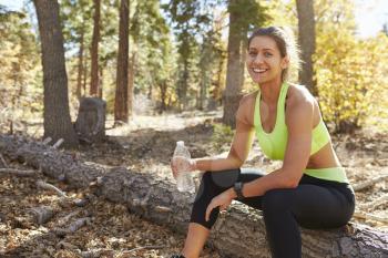 Female runner in a forest takes a break, looking to camera