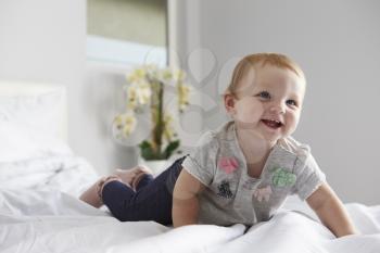 A happy baby girl crawling on a bed, copy space on left