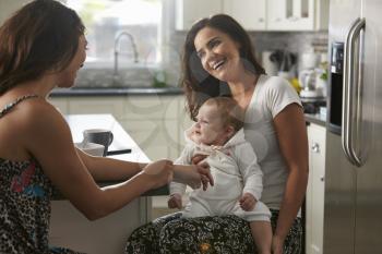 Female couple sitting in the kitchen with baby girl on knee