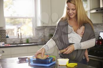Mum preparing lunchbox while baby sleeps on her in a carrier