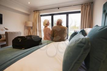 Senior Couple On Vacation Sitting On Hotel Bed