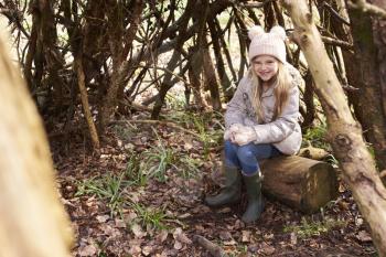 Young girl sitting in a forest shelter made of tree branches