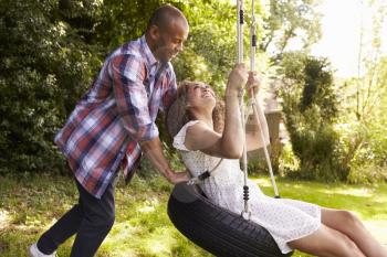 Man Pushing Woman On Tire Swing In Garden