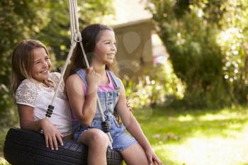 Side View Of Two Girls Playing On Tire Swing In Garden