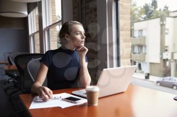 Thoughtful Businesswoman Working On Laptop By Window