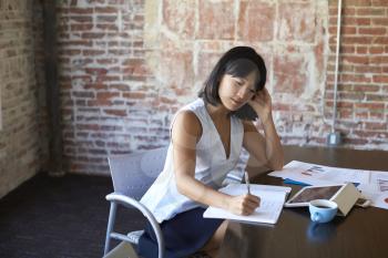 Businesswoman Making Notes On Document In Boardroom