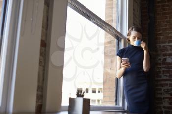 Businesswoman Checking Phone Standing By Office Window