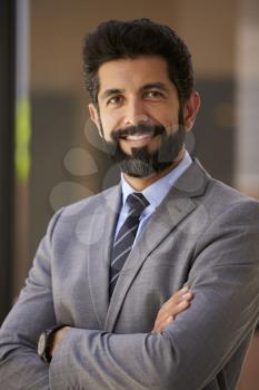 Smiling Hispanic businessman, arms crossed, close up vertical