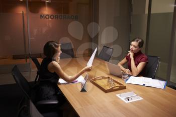 Two businesswomen working late in office look at documents