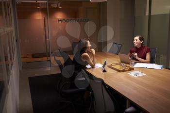 Two businesswomen working late in an office share a joke