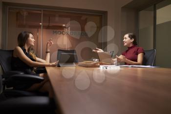 Two businesswomen working late in an office talking