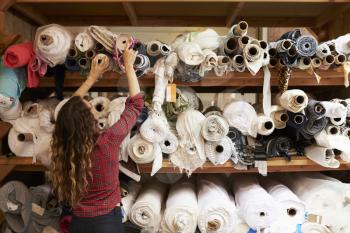 Young woman reaching to select fabric from storage shelves