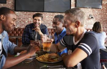Male Friends Eating Out In Sports Bar With Screens In Behind