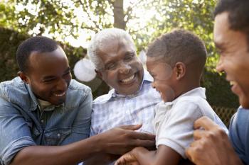 Black grandfather, sons and grandson talking in a garden
