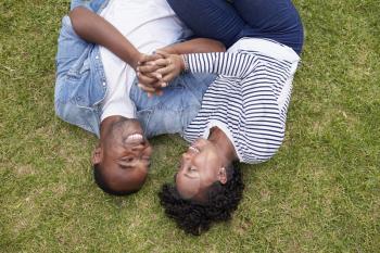 Young black couple lying on grass look at each other, aerial