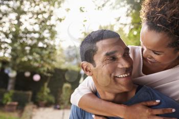 Young black couple piggyback in garden looking at each other
