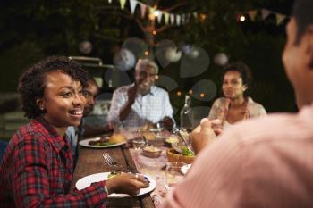 Adult black family eat dinner in garden, over shoulder view