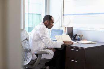 Doctor Wearing White Coat Reading Notes In Office