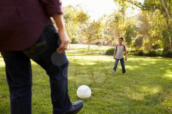 Dad kicking football to seven year old son in a park, crop