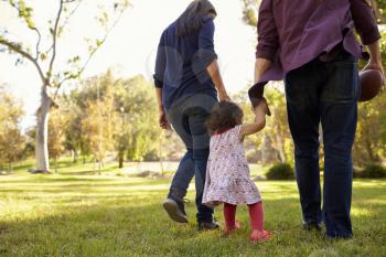 Couple walking in park with their young daughter, back view