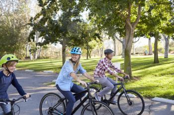 Parents and young son cycling through a park, close up