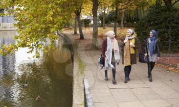 British Muslim Female Friends Walking By River In City