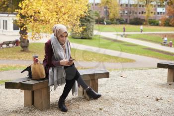 British Muslim Woman Texting On Mobile Phone In Park