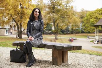 British Muslim Woman Sitting On Bench In Park