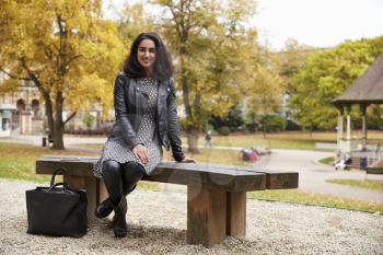 Portrait Of British Muslim Woman Sitting On Bench In Park