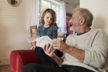 Grandfather And Granddaughter At Home Looking At Photographs