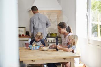 Kids and mum at table, dad cooking, three quarter length