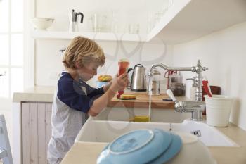 Boy squeezing washing up liquid into sink to wash dishes