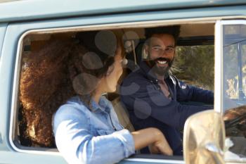 Couple driving camper van smiling at each other