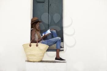 Young woman on holiday sitting on steps reading a guidebook