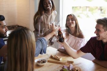 Five happy friends make a toast at a kitchen dinner party