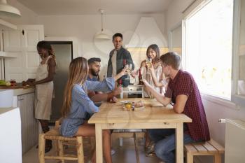 Friends making a toast in kitchen, one preparing food