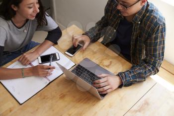 Teen couple study using laptop and phones, elevated close up